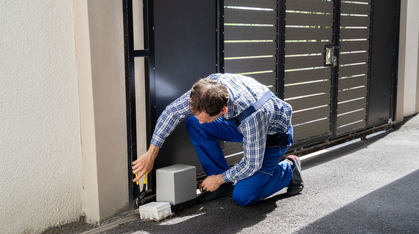 Technicien installateur ajustant le bras articulé d'une motorisation de portail battant aluminium, outils au sol, chantier résidentiel en Bretagne